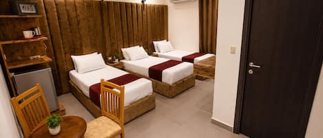 Une chambre d’hôtel avec deux lits, une petite table avec des chaises, une plante, un réfrigérateur et une porte.