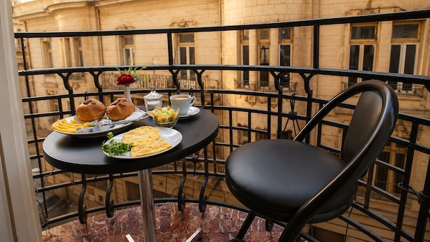 A balcony with a table set for breakfast, including croissants, a muffin, and a fruit bowl.