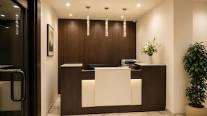 A reception desk with a dark wood finish, a white counter, and a potted plant to the right.