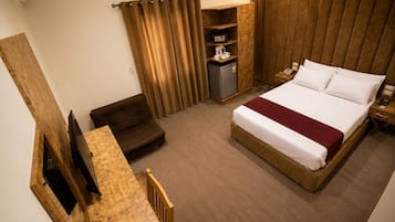 A hotel room with a bed, a sofa, a small table, a cabinet, and a curtain.