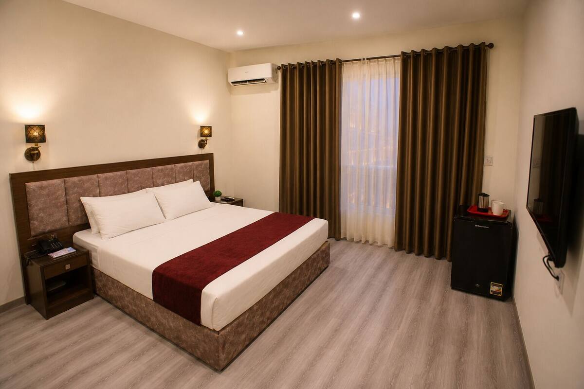Una habitación de hotel con cama, mesitas de noche, aire acondicionado, televisor y cortinas.