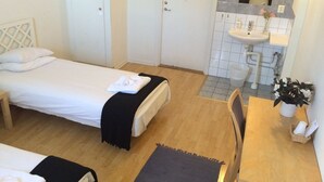 A hotel room with two beds, a wooden floor, a small table with a chair, a sink, and a mirror. - Hotell Östergyllen (Linkoping)