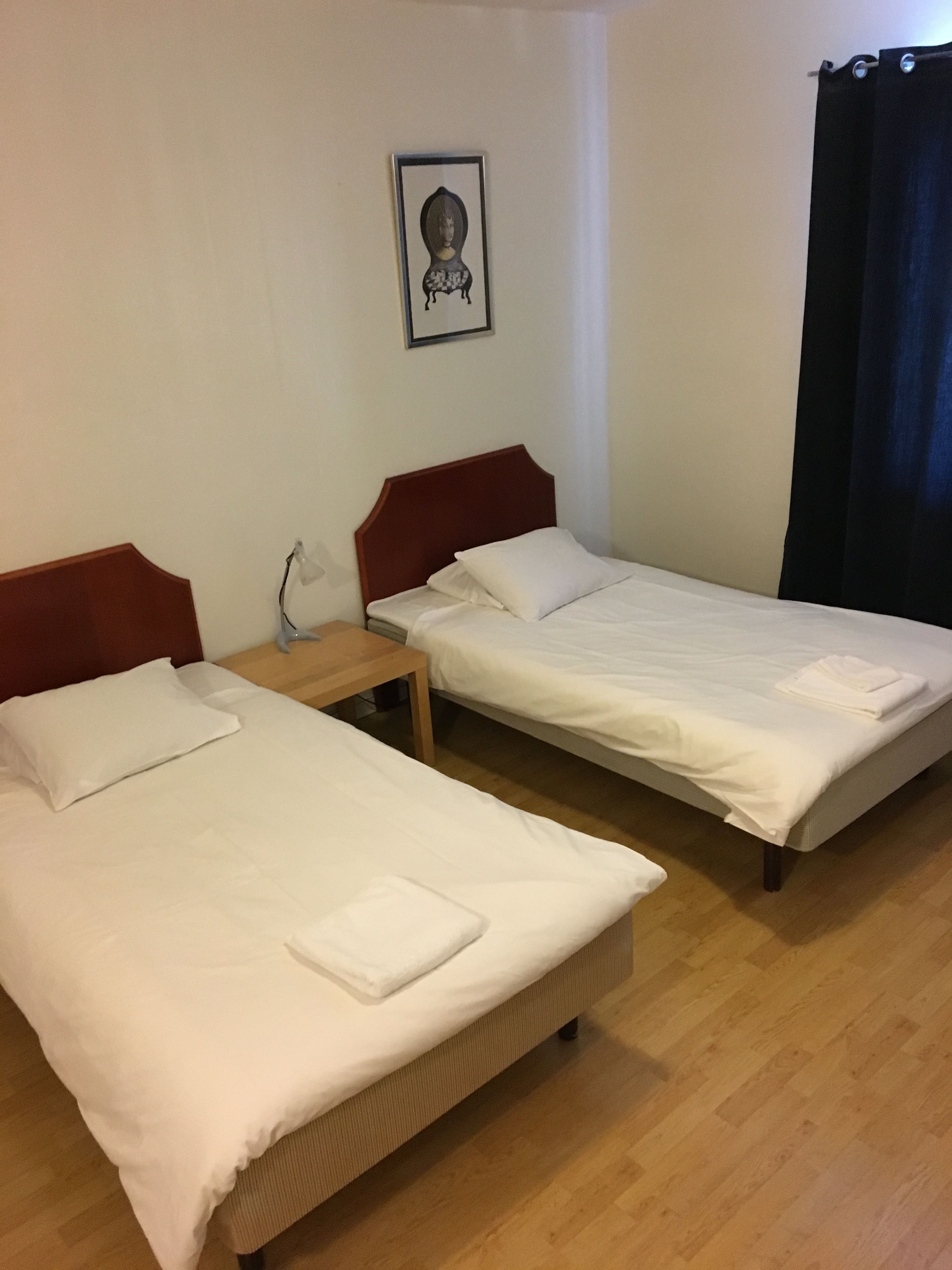 A hotel room with two single beds, a small table, and a wall-mounted picture.