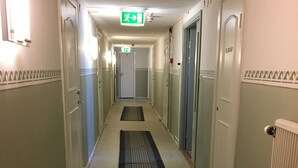 A hotel hallway with a central walkway, doors on both sides, and a green exit sign. - Hotell Östergyllen (Linkoping)