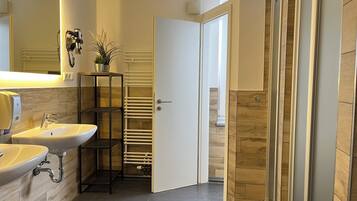 A modern bathroom with two sinks, a mirror, a towel rack, and a door leading to another room.