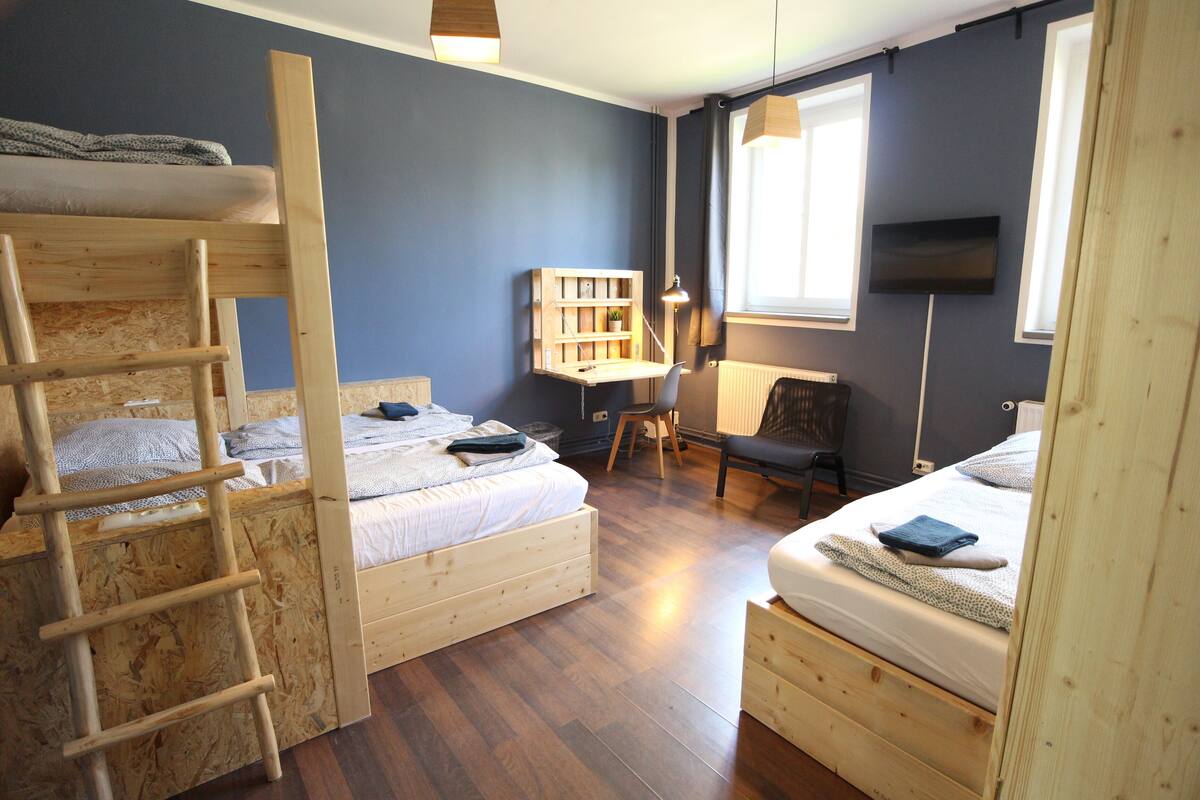 A bedroom with two wooden bunk beds, a desk with a chair, a bookshelf, and a television on the wall.