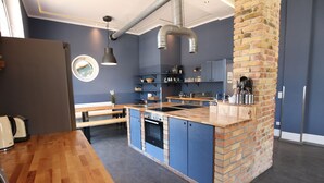 A modern kitchen with a central island, built-in oven, and a brick accent wall. - Blue Doors Hostel KTV (Rostock)