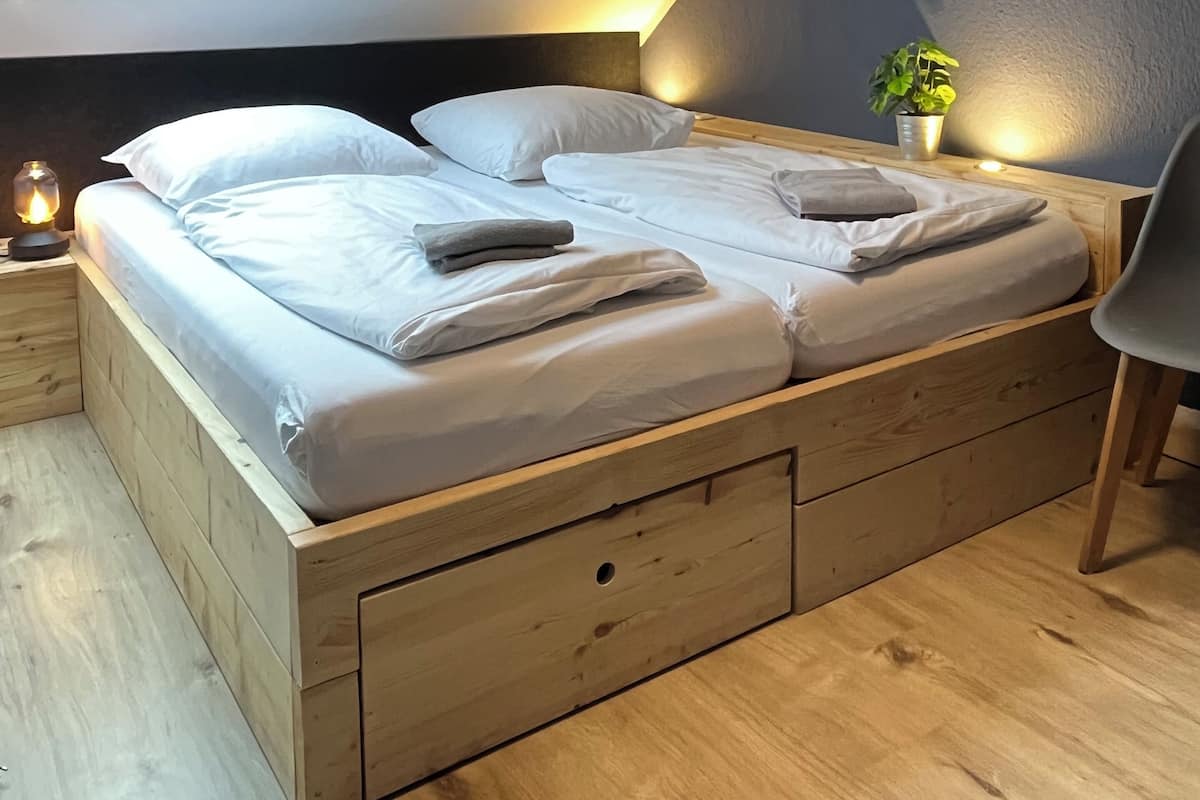 A neatly made bed with white linens, a bedside lamp, and a small potted plant on the nightstand.