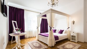 A bedroom with a four-poster bed, a bedside table, a nightstand, a round table with a mirror, and a chandelier. - Vila Marioara (Sibiu)