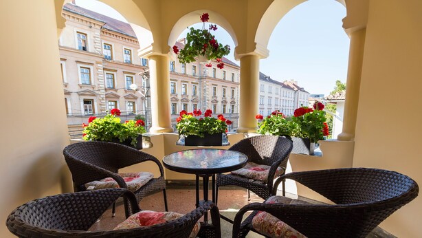 A balcony with wicker chairs and a table, overlooking a building with large windows. - Vila Marioara (Sibiu)