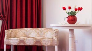 A room with a patterned sofa, a white table with a vase of red and white tulips, and red curtains. - Vila Marioara (Sibiu)