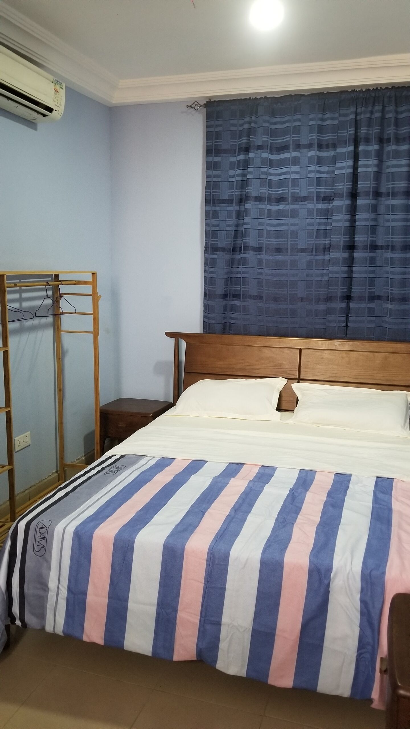 A bedroom with a wooden bed, a nightstand, a wardrobe, and an air conditioning unit on the wall.