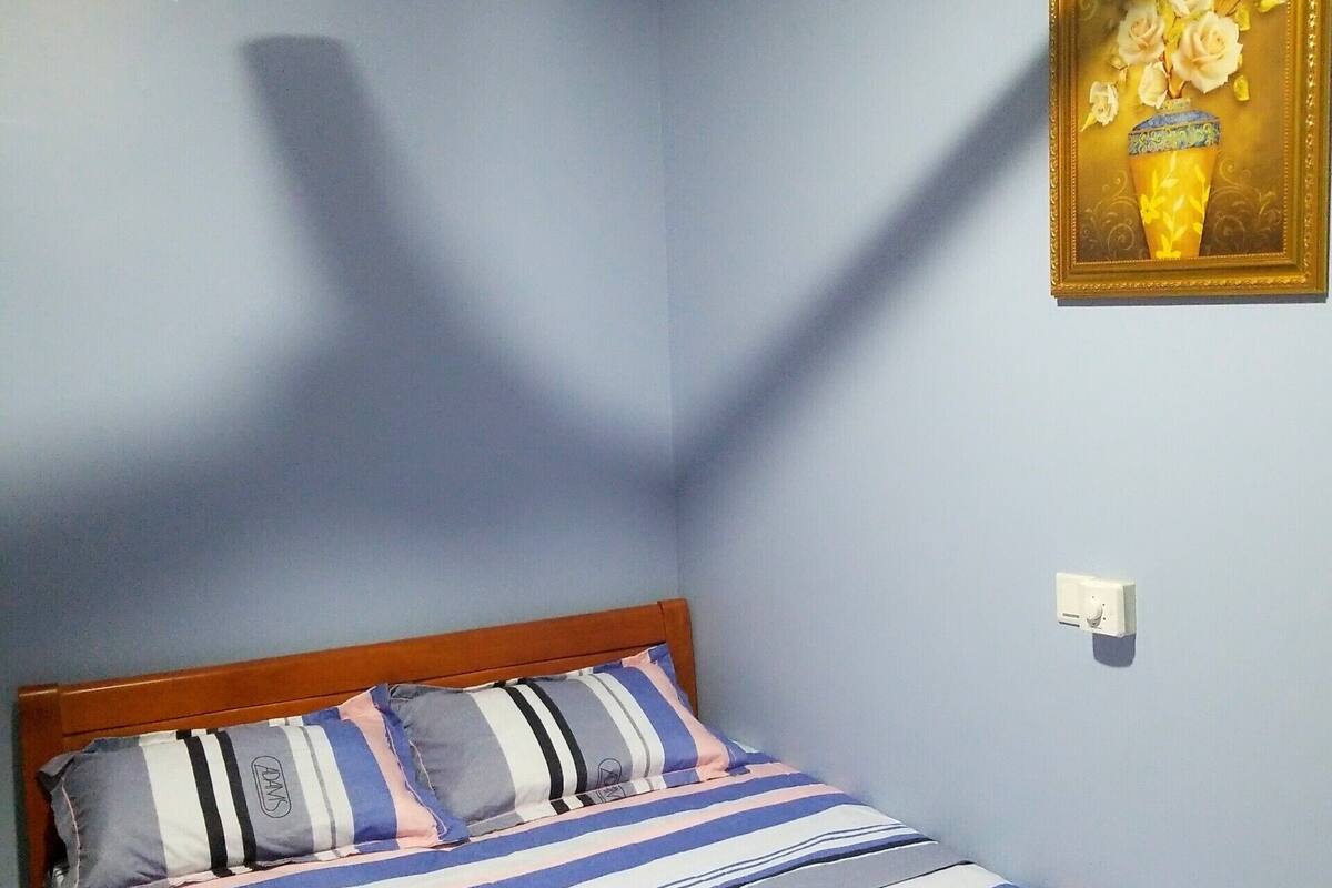 A bedroom with a bed, a ceiling fan, and a framed picture on the wall.