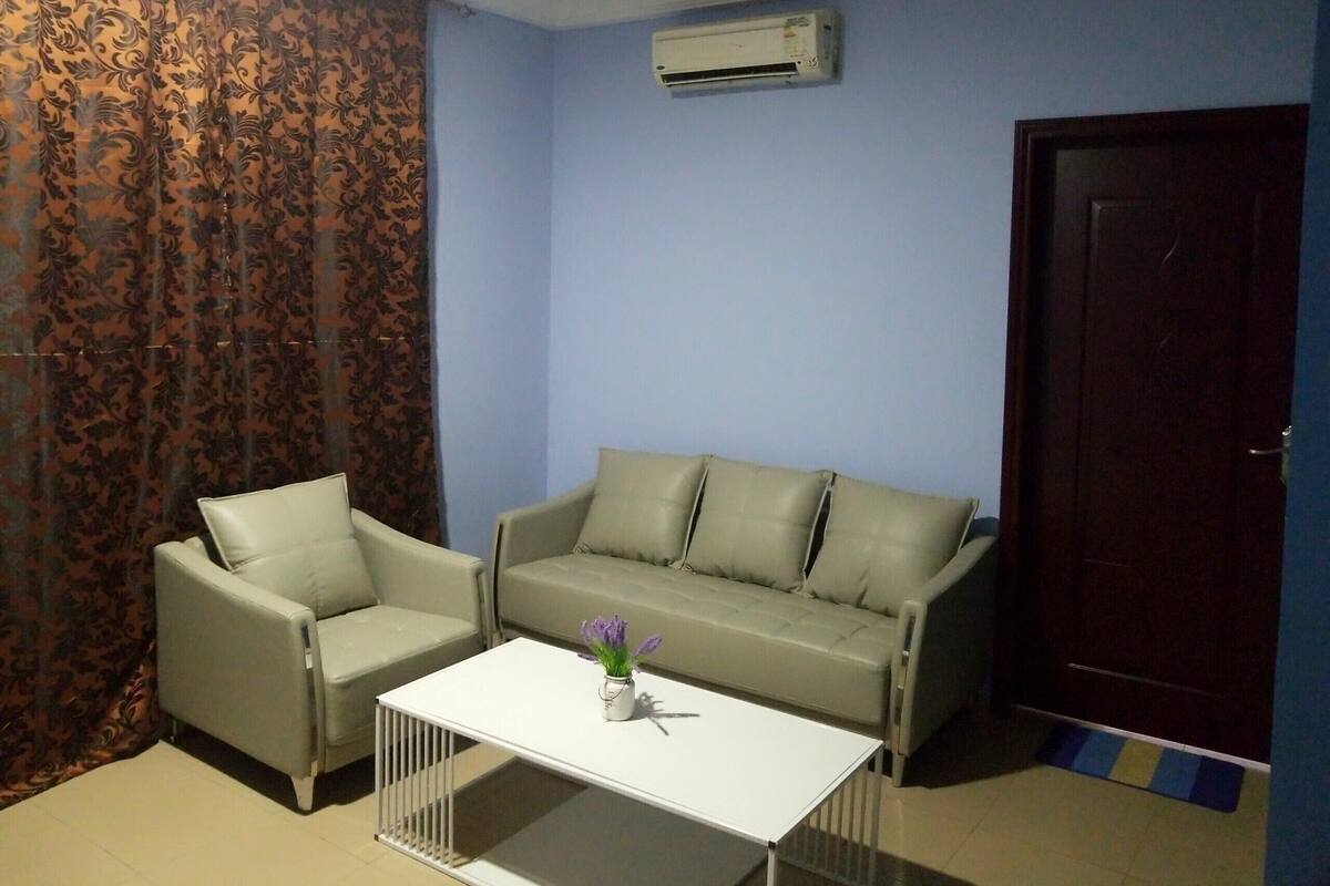 A living room with a beige sofa, a white coffee table, and a patterned curtain.