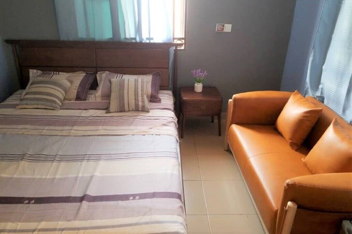 A bedroom with a bed, a nightstand, a leather sofa, and a window with curtains.