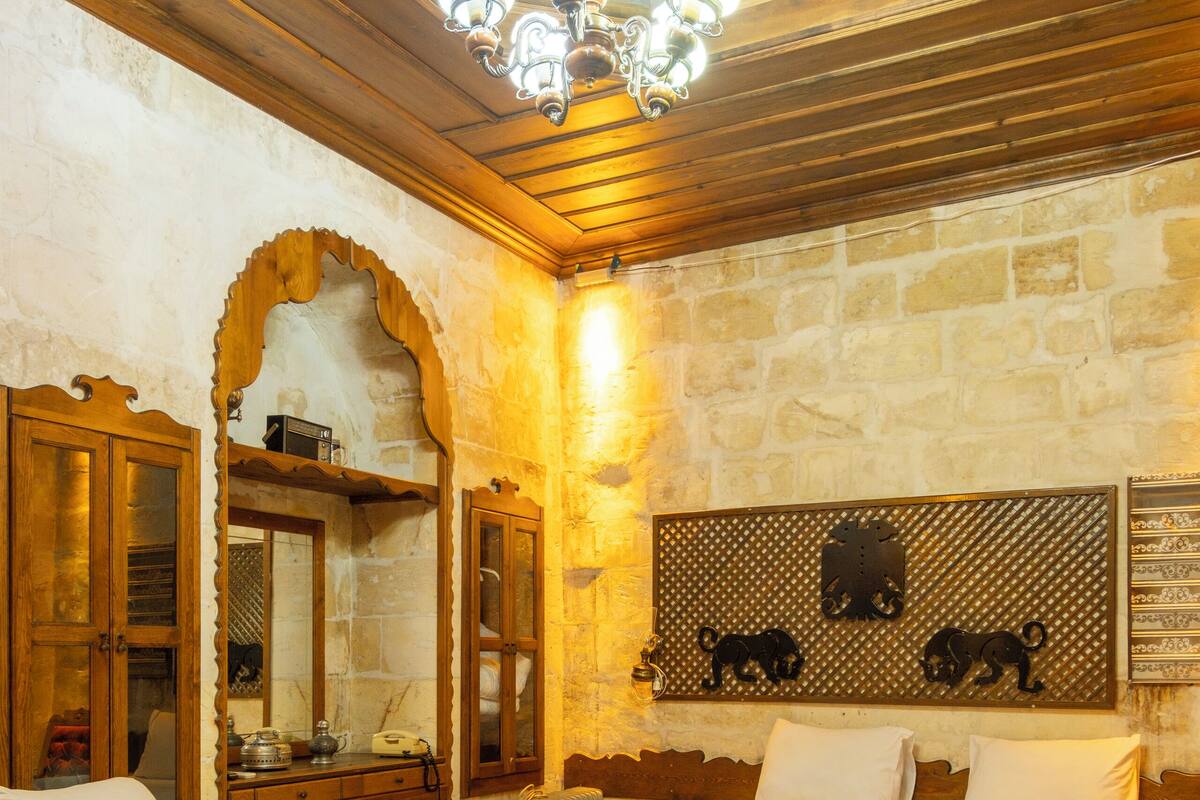 A hotel room with two beds, wooden ceiling, stone walls, and a chandelier.