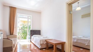 Hotellihuone, jossa on sänky, sohva, pieni pöytä ja parveke, jolta on näkymä vehreään maisemaan.