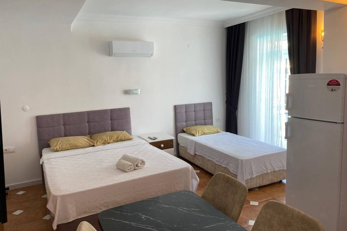 Une chambre d’hôtel avec deux lits, une table à manger, un réfrigérateur et une fenêtre avec des rideaux.