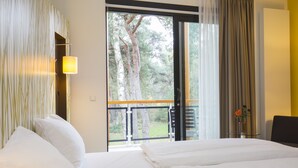 A hotel room with a bed, a desk, and a view of trees through a large window. - Landgoed ISVW (Leusden-Centrum)