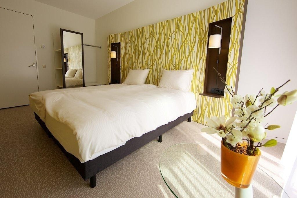 Una habitación de hotel moderna con una cama grande, una mesita de vidrio y una planta en maceta.