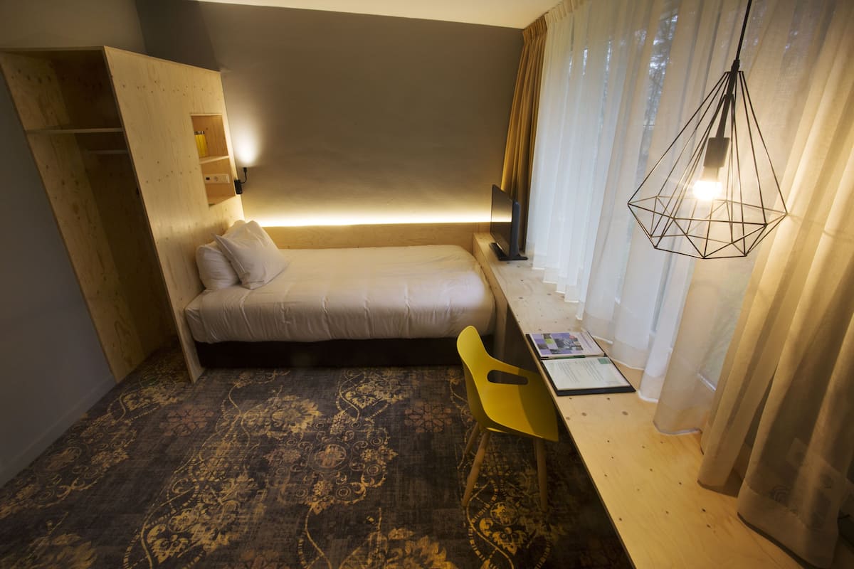 A compact bedroom with a bed, a desk, a chair, and a hanging light fixture.