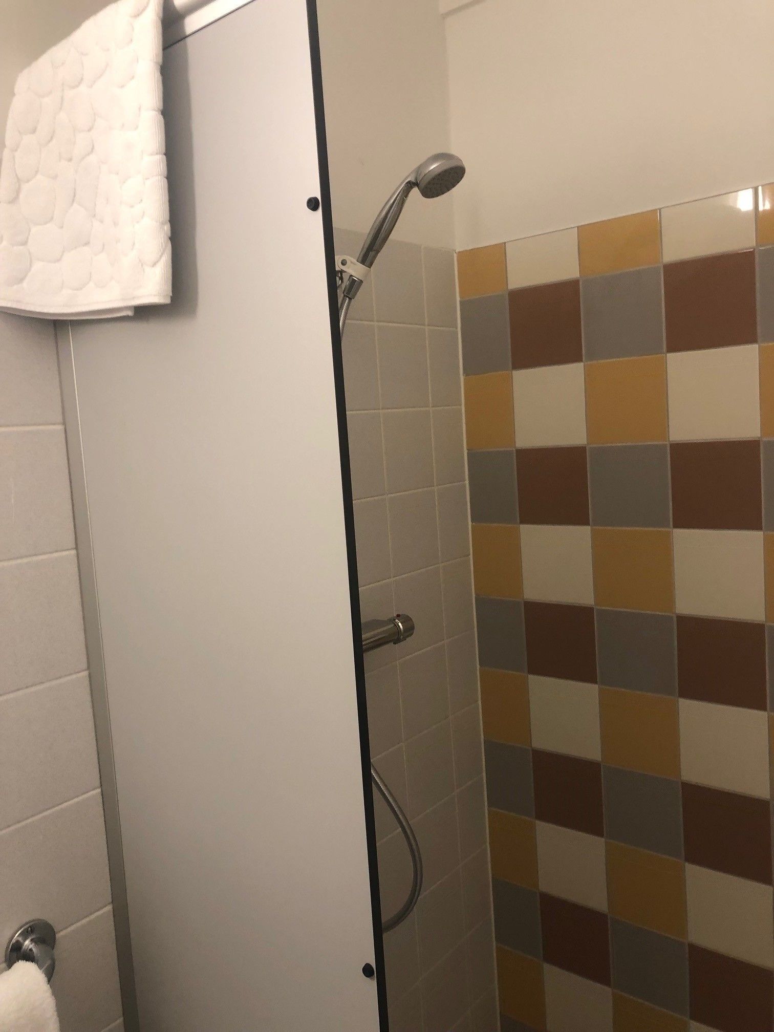 A bathroom with a shower, tiled walls, and a towel hanging on the door.