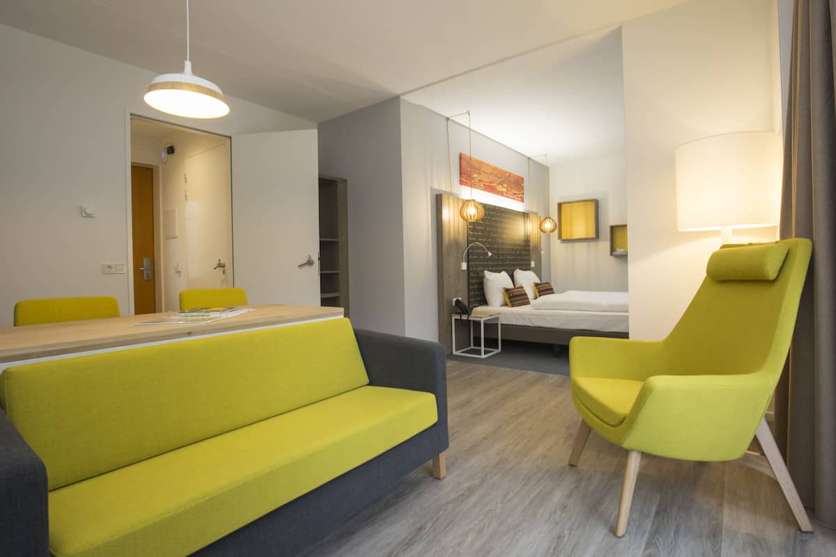 A modern hotel room with a dining area, a sofa, a chair, and a bed.