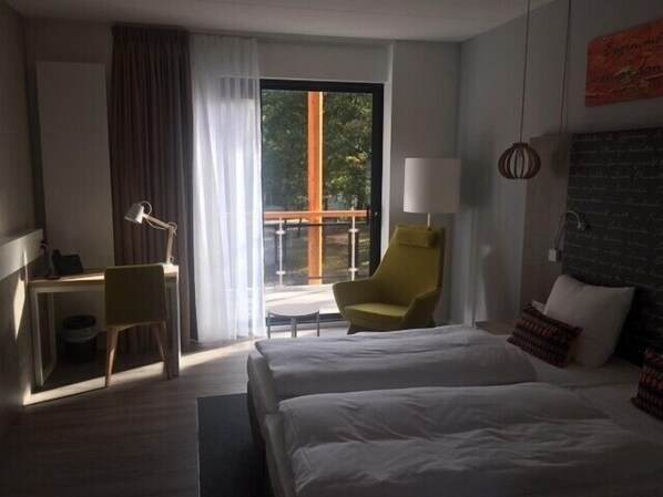 Habitación de hotel con cama, escritorio, silla, ventana con cortinas y vista a zonas verdes.