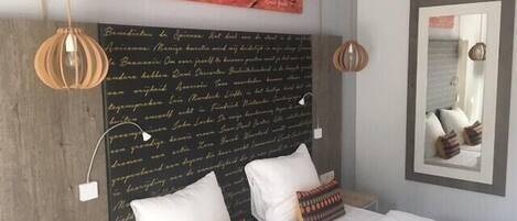 Un dormitorio con una cama grande, dos almohadas, una pared con una cita y un espejo.