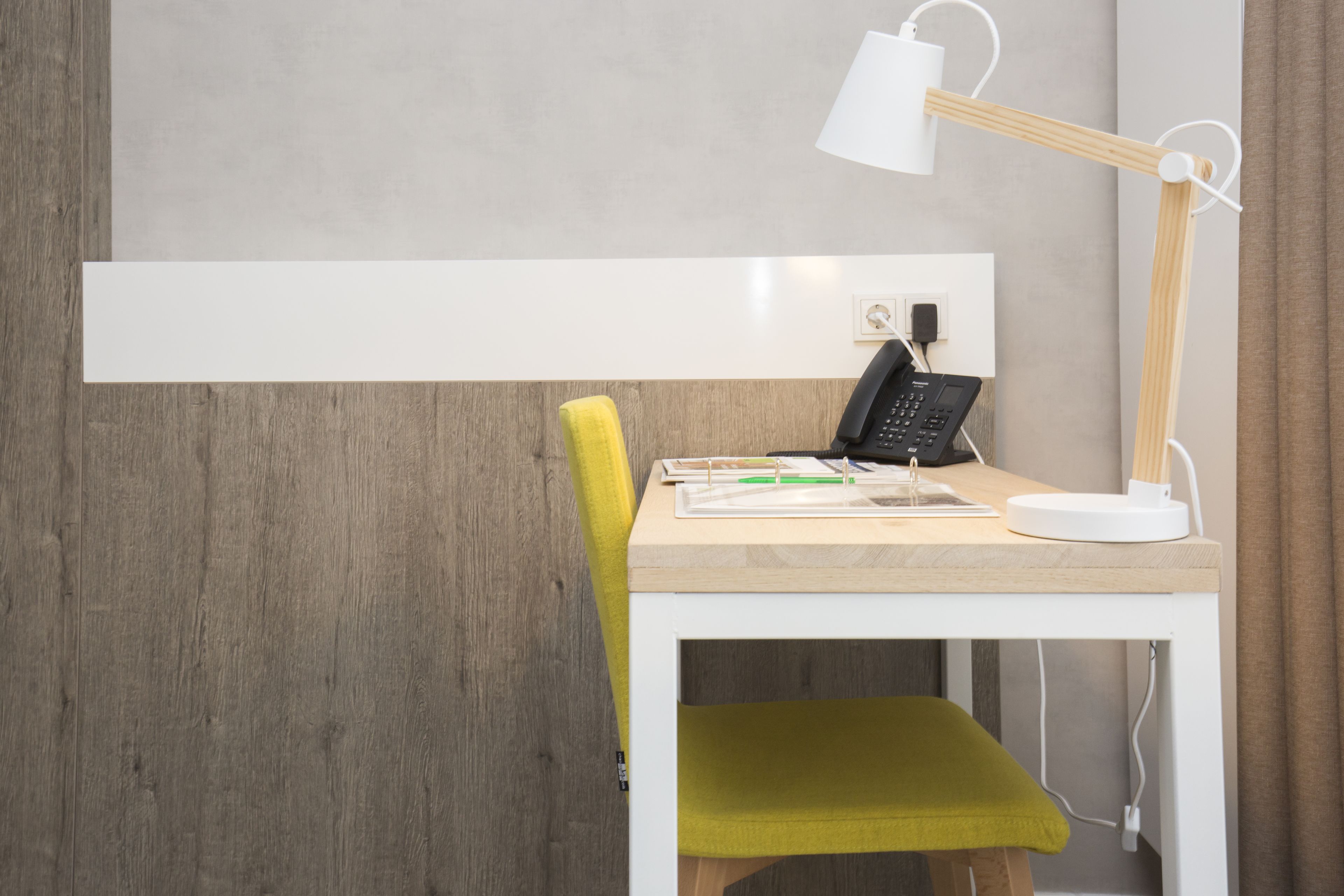 Un espace de travail moderne avec un bureau en bois, une chaise jaune, une lampe de bureau blanche et un téléphone.