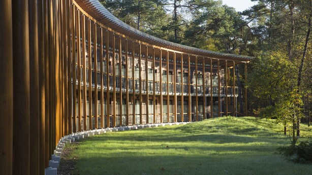 A modern building with a curved wooden facade and a glass balcony overlooking a grassy area. - Landgoed ISVW (Leusden-Centrum)