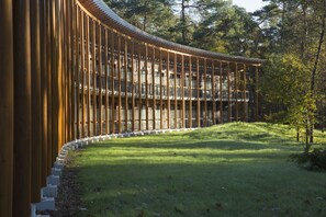 A modern building with a curved wooden facade and a glass balcony overlooking a grassy area. - Landgoed ISVW (Leusden-Centrum)
