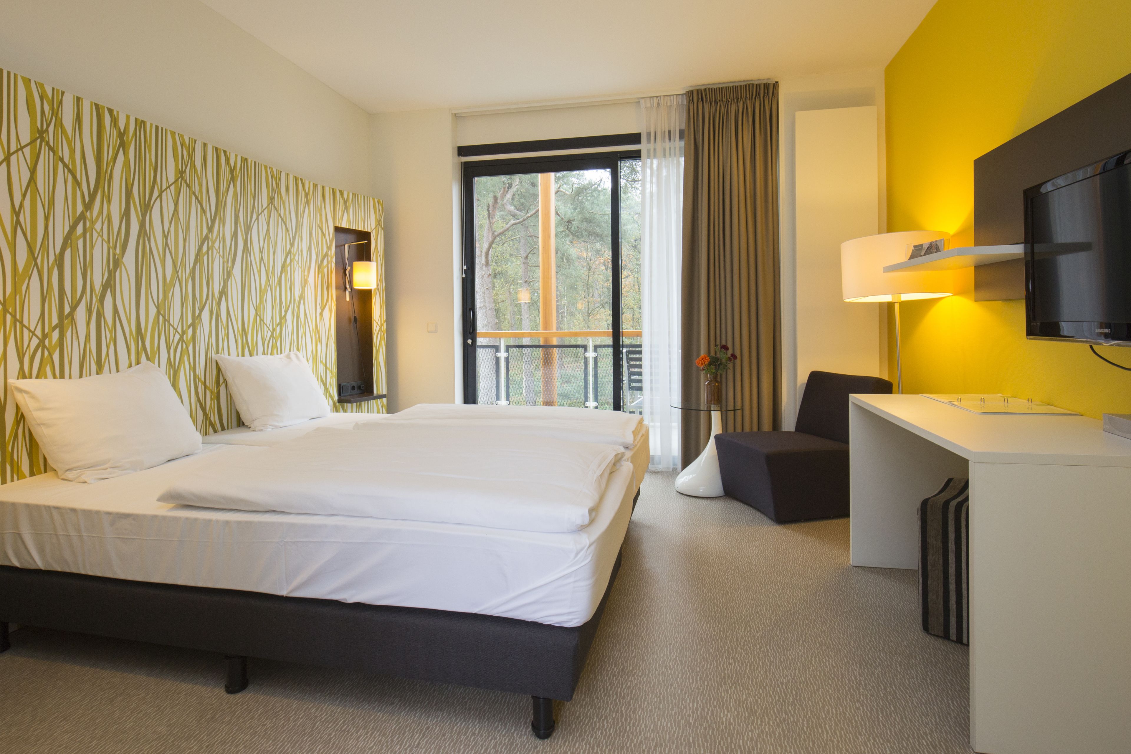 A hotel room with a large bed, a desk, a chair, and a TV.