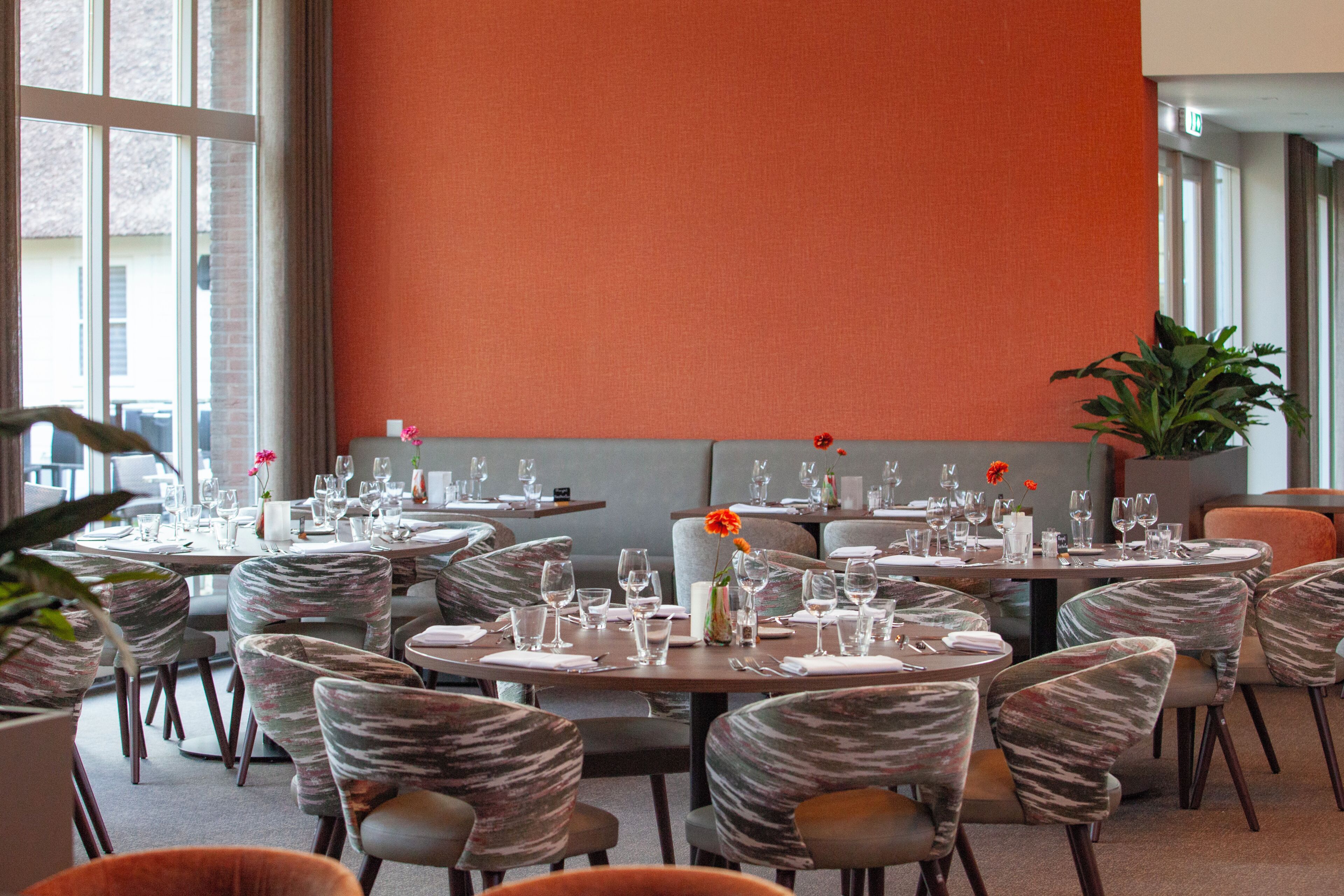 Un restaurante con mesas redondas, sillas acolchadas y un amplio ventanal.