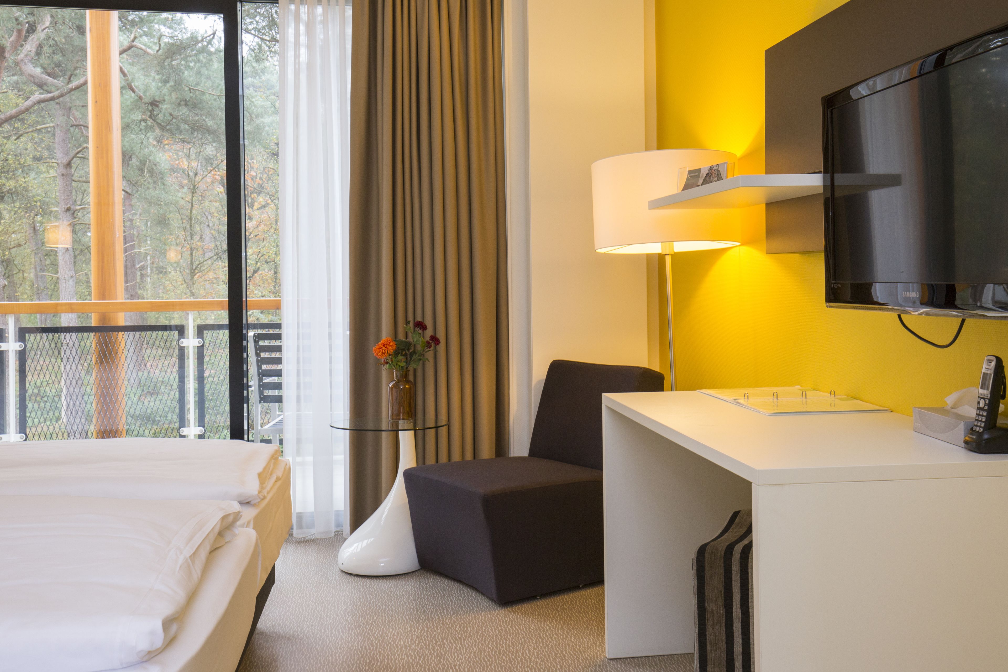 Una habitación de hotel con cama, escritorio, silla, televisor y ventana con cortinas.