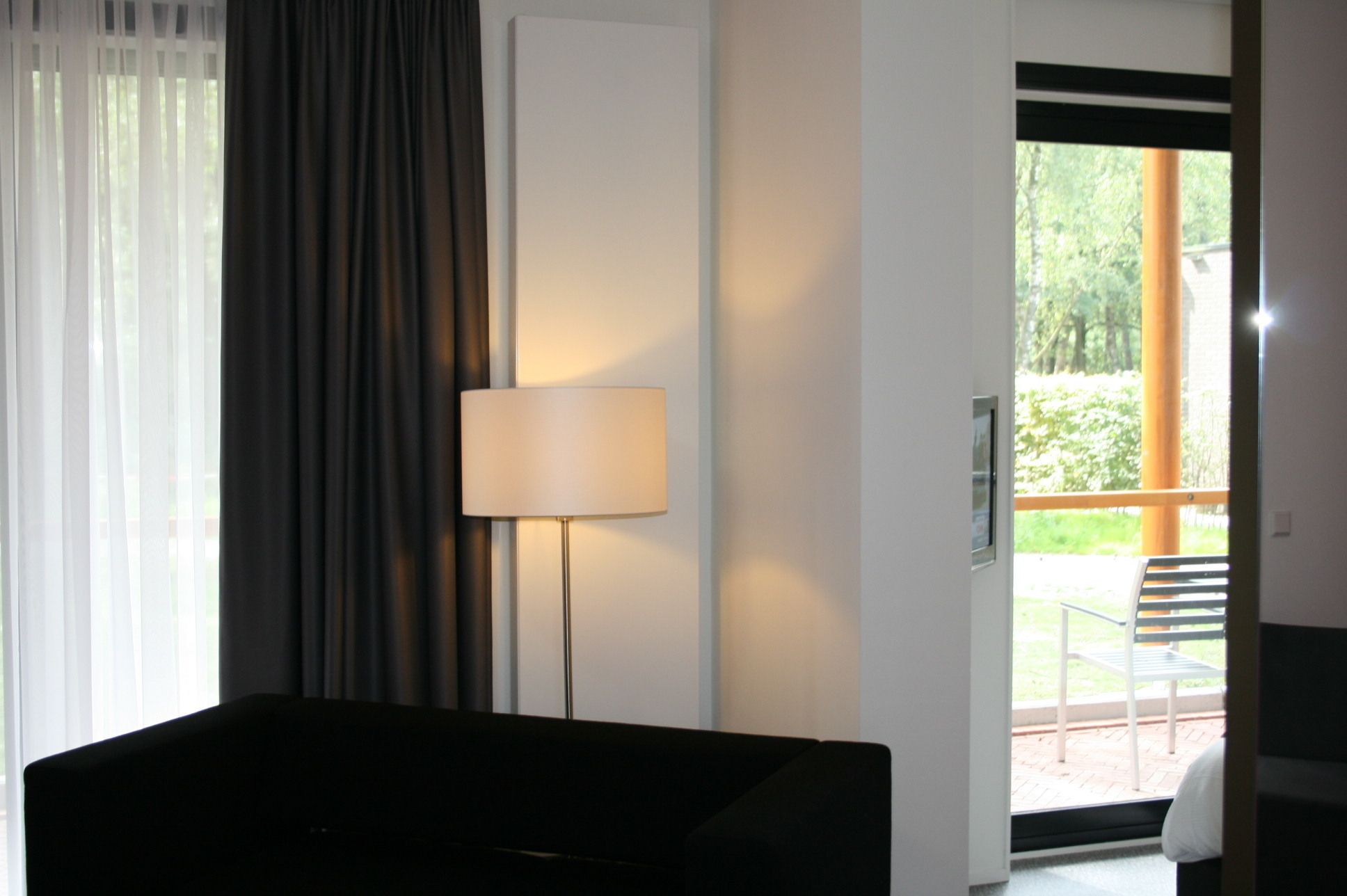 A hotel room with a bed, a lamp, a door, and a view of the outside.