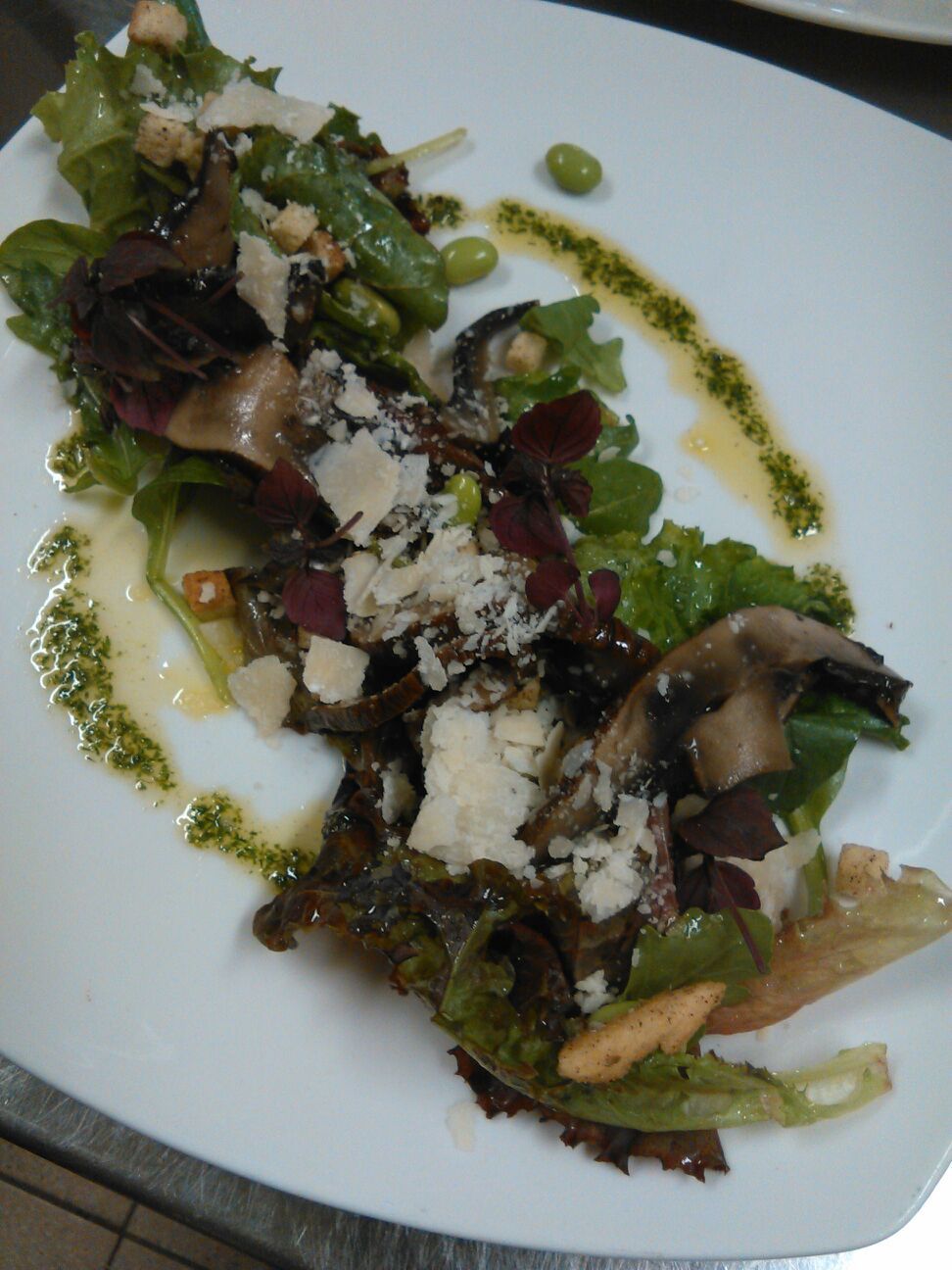 Un plato de comida con diferentes vegetales verdes, champiñones y queso desmenuzado.