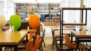 A library with wooden tables and chairs, a bookshelf in the background, and a vase with flowers on a table. - Landgoed ISVW (Leusden-Centrum)
