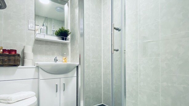 A modern bathroom with a glass shower enclosure, white cabinetry, and a sink with a mirror above it. - Seafield Seafront Apartments (Hove)