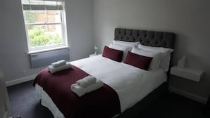 A neatly made bed with a grey headboard, white and red bedding, and two white towels on the bed. - 3 Summertown Court (Oxford)