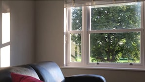 A room with a black leather sofa, a red pillow, and a window with a view of trees. - 3 Summertown Court (Oxford)