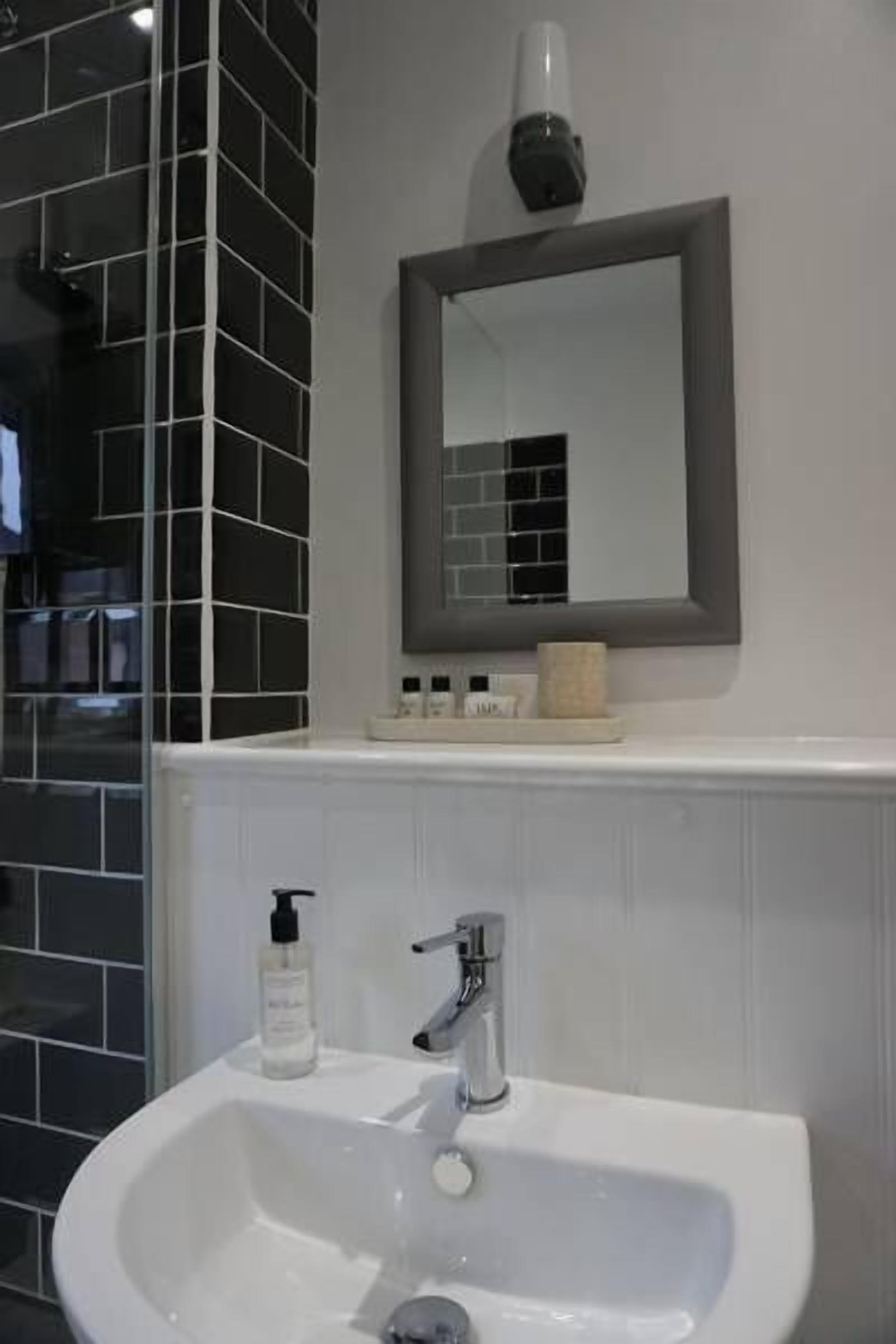 A bathroom with a white sink, a mirror, and a soap dispenser.