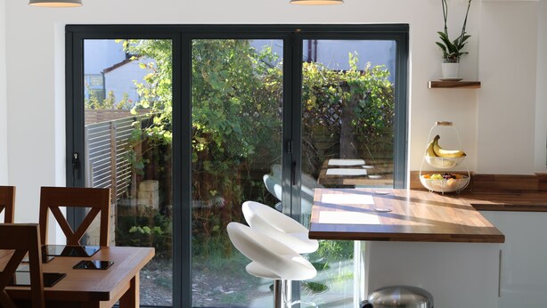 A modern kitchen with a wooden countertop, a glass door leading to a garden, and a hanging plant. - Luxury Victorian Garden Apartment (Bristol)