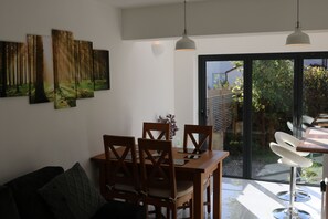 A dining area with a wooden table and chairs, a sofa, and a large window with a view of greenery.