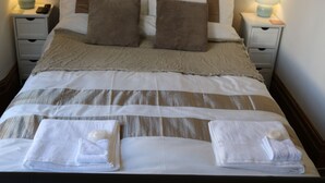 A neatly made bed with a striped bedspread, two pillows, and two folded towels on the foot of the bed. There are two bedside tables with lamps and a remote control on one of them. - Luxury Victorian Garden Apartment (Bristol)