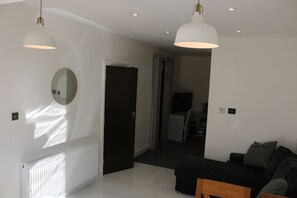 A modern living room with a sofa, a coffee table, and a TV. There is a door leading to another room, and a radiator on the wall.