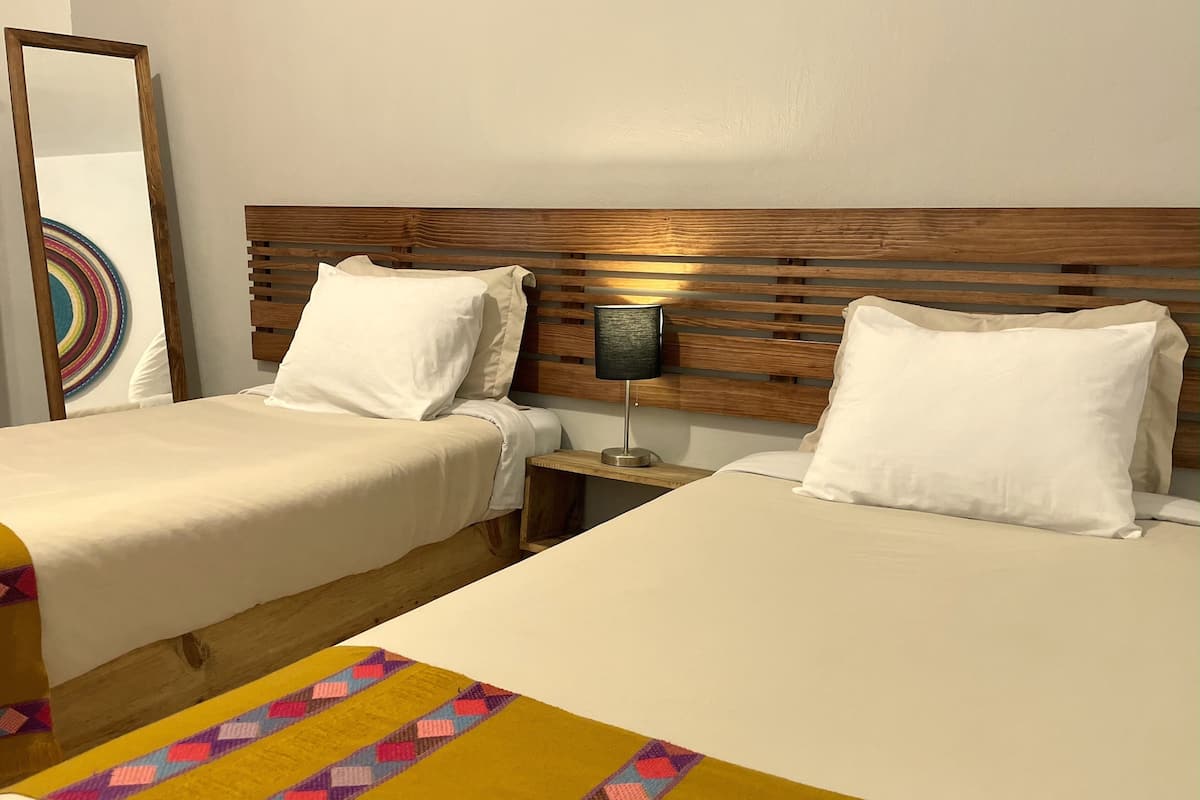 Habitación de hotel con dos camas, cabecero de madera, lámpara de noche y una alfombra colorida.