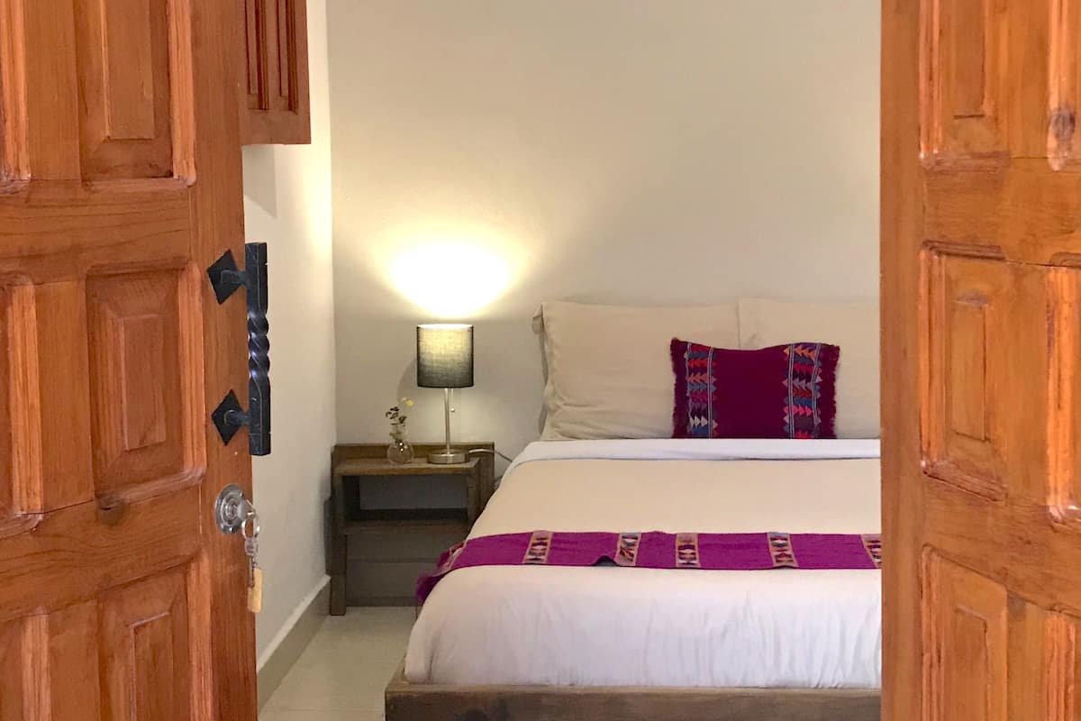 Un dormitorio con una cama, una mesita de noche, una lámpara y una puerta de madera.