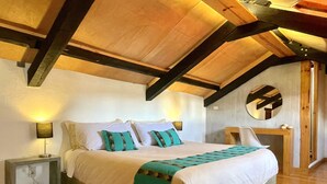 Un dormitorio con una cama grande, vigas de madera, un espejo redondo y una mesita de noche con lámpara.
