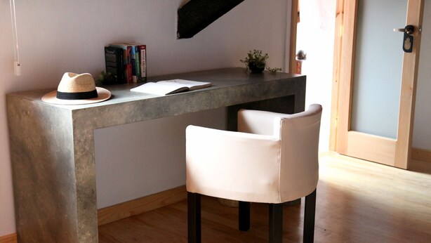 Un espacio de trabajo moderno con un escritorio de hormigón, una silla blanca y un sombrero sobre el escritorio.